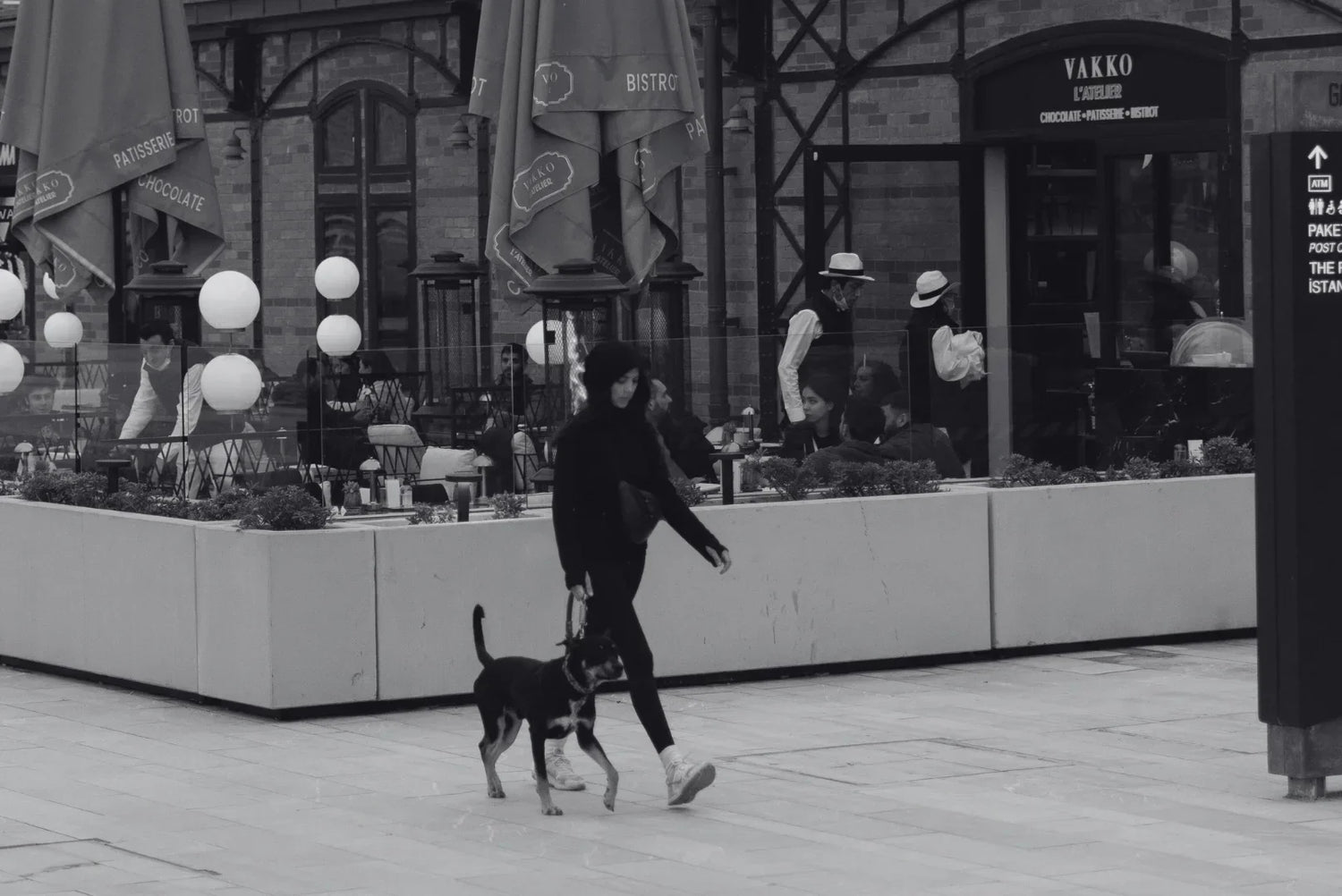 Frau führt ihren Hund ruhig an der Leine durch eine belebte Straße vor einem Café